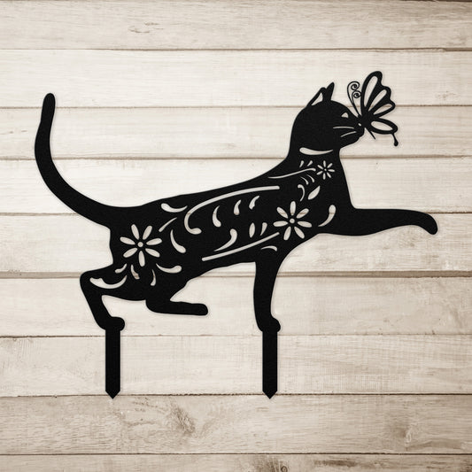 A black yard/garden stake of a cat with a butterfly on it nose and floral elements on it body.