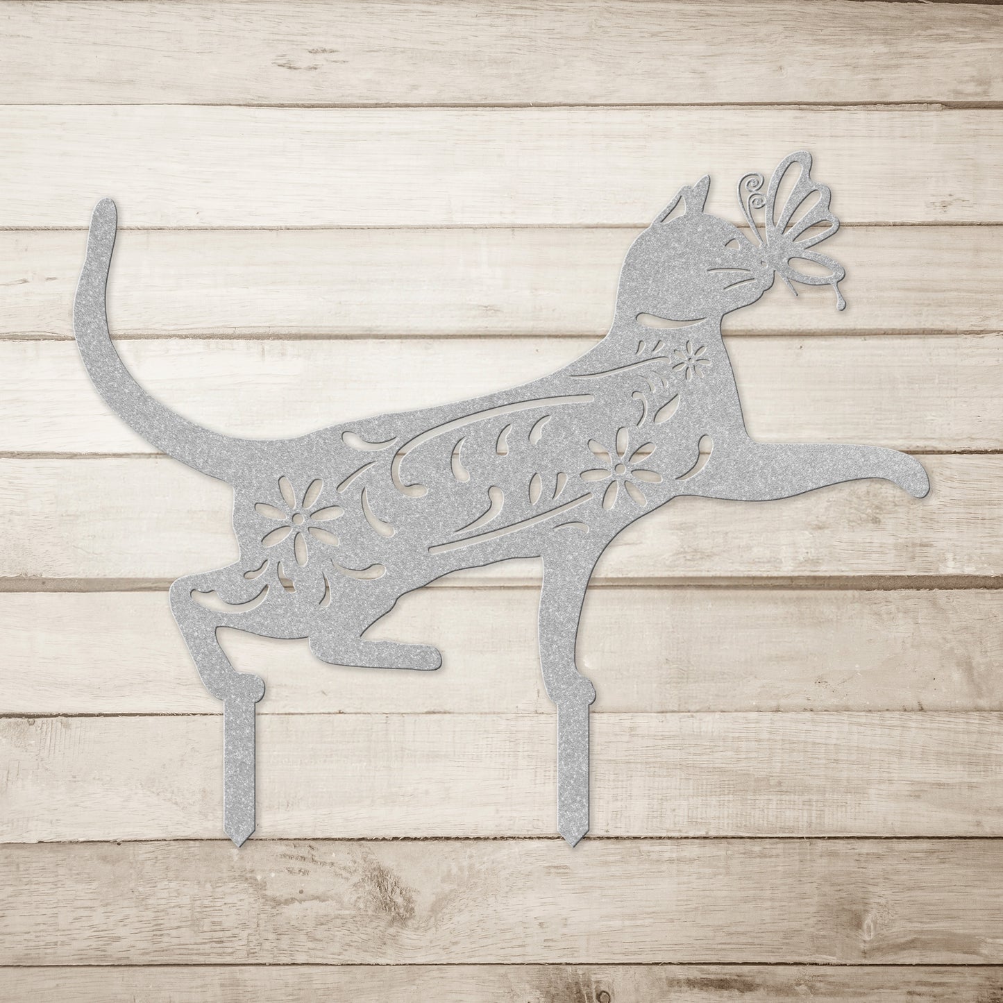 A silver yard/garden stake of a cat with a butterfly on it nose and floral elements on it body.