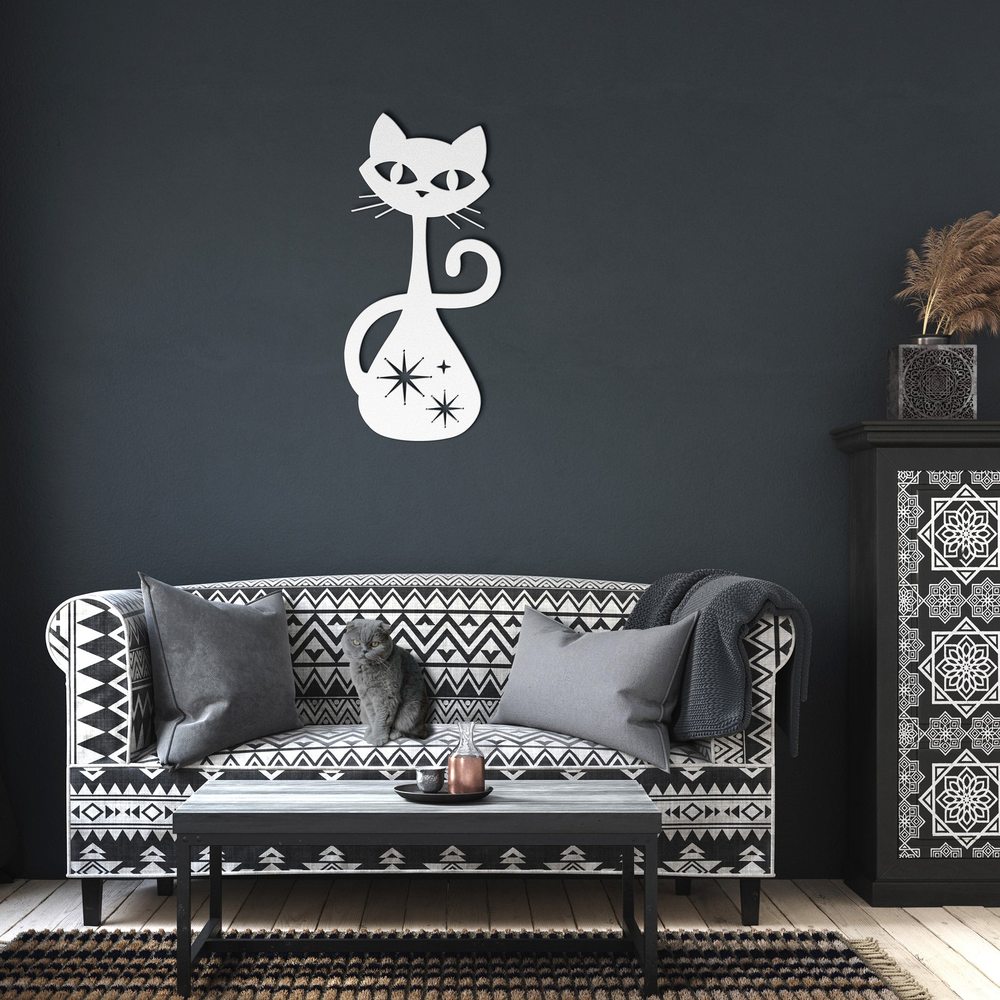 A white atomic cat metal wall art hanging in a dark living room.