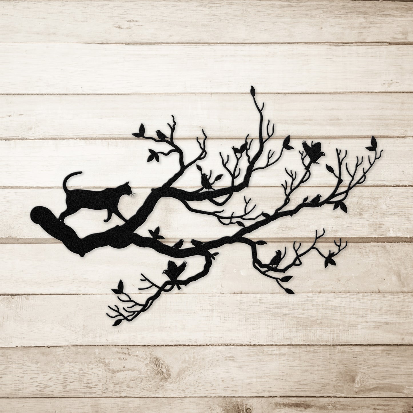A black metal wall art decor of a cat stalking birds on a branch on a simple wood background.