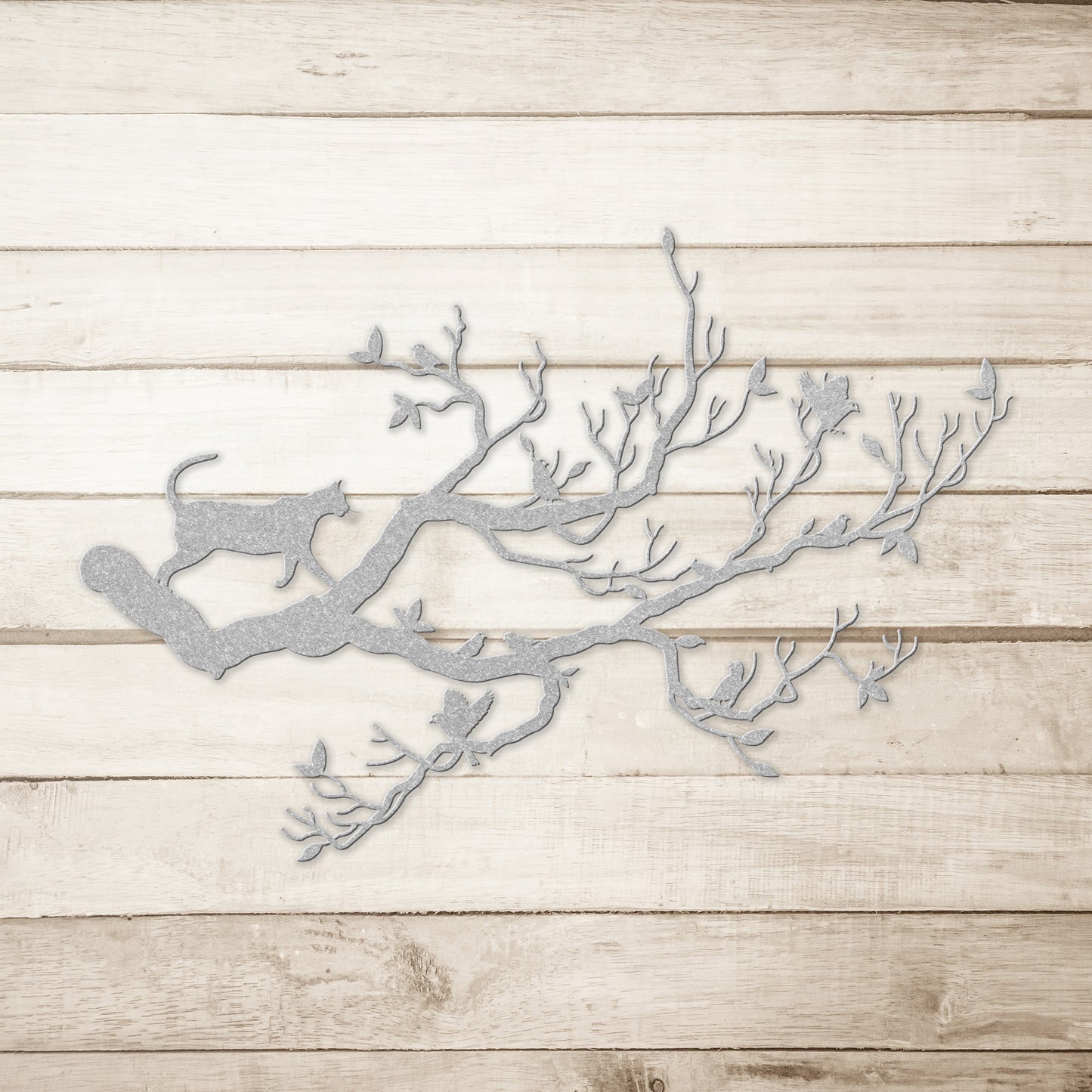 A silver metal wall art decor of a cat stalking birds on a branch on a simple wood background.