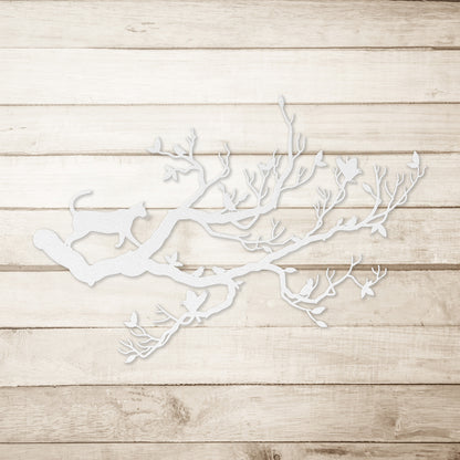 A white metal wall art decor of a cat stalking birds on a branch on a simple wood background.