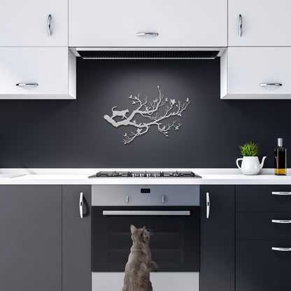 A metal wall art decor of a cat stalking birds on a branch hanging in a dark kitchen.