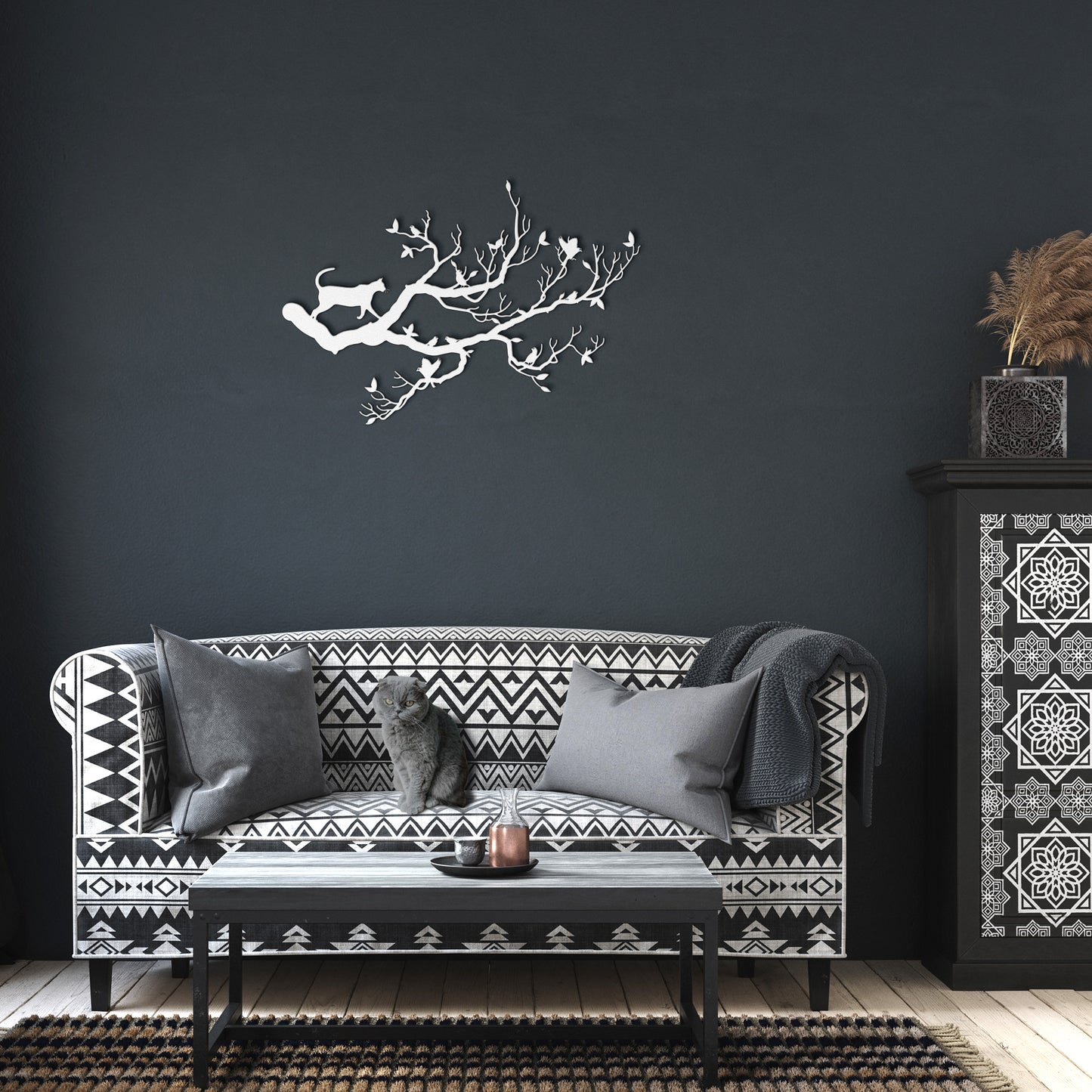 A white metal wall art decor of a cat stalking birds on a branch hanging in a dark living room.