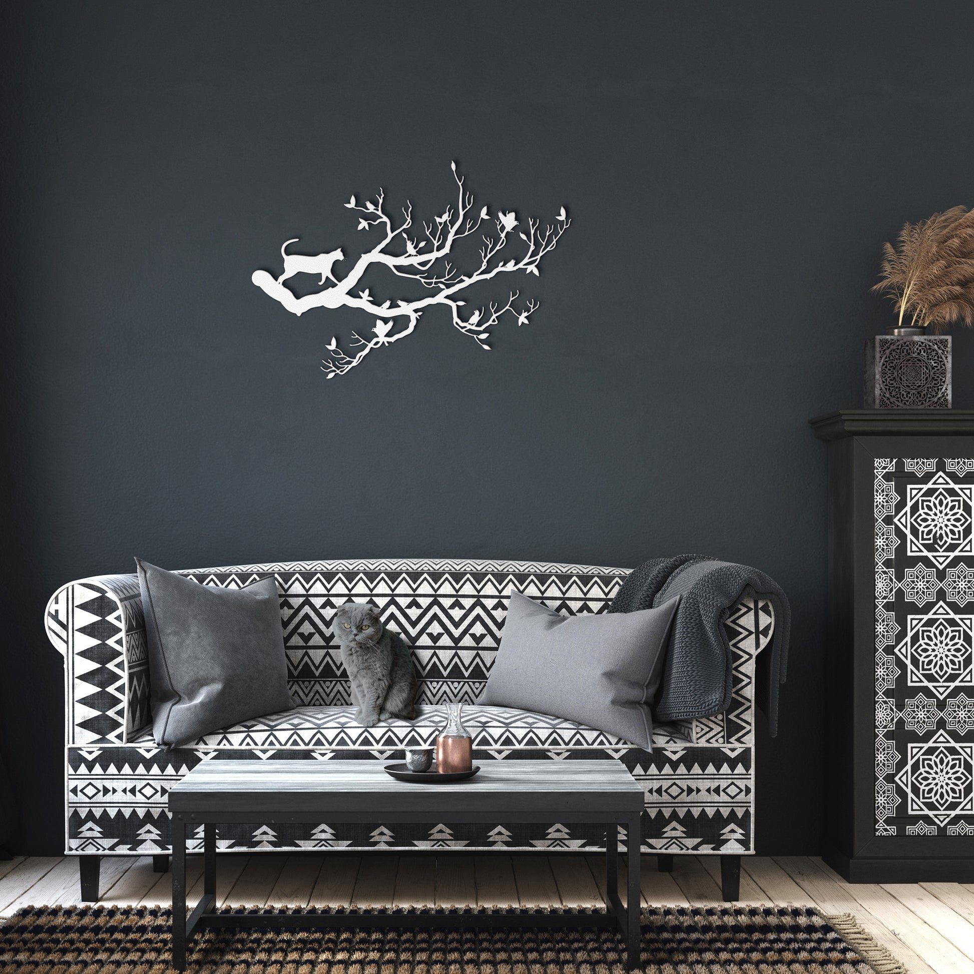A white metal wall art decor of a cat stalking birds on a branch hanging in a dark living room.