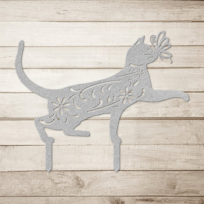 A silver yard/garden stake of a cat with a butterfly on it nose and floral elements on it body.