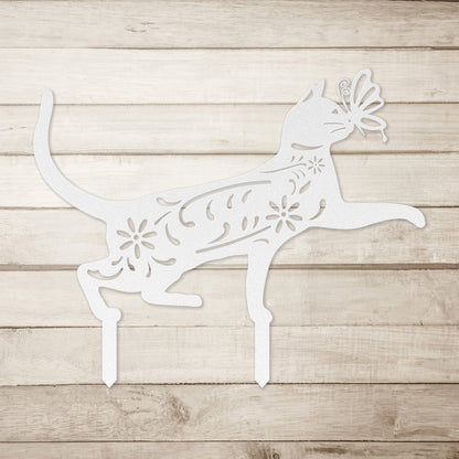A white yard/garden stake of a cat with a butterfly on it nose and floral elements on it body.