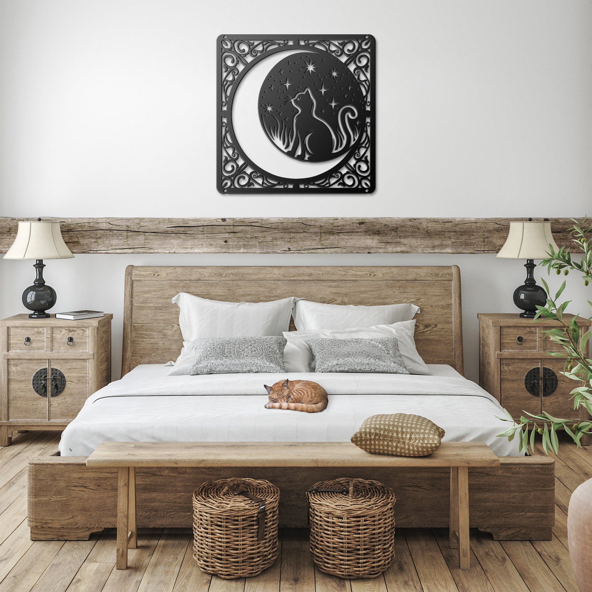 A black home decor metal sign of a cat inside a crescent moon next to a field of stars. All of this is bordered by floral vines. It hangs in a farmhouse bedroom above an orange tabby cat.
