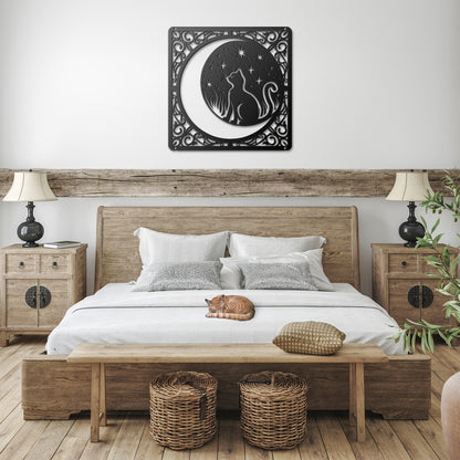 A black home decor metal sign of a cat inside a crescent moon next to a field of stars. All of this is bordered by floral vines. It hangs in a farmhouse bedroom above an orange tabby cat.