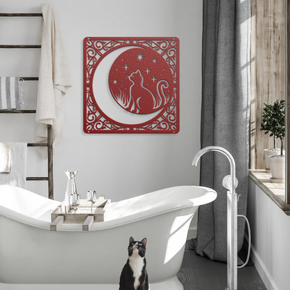 A red home decor metal sign of a cat inside a crescent moon next to a field of stars. All of this is bordered by floral vines. It hangs in a modern bathroom above a tuxedo cat.