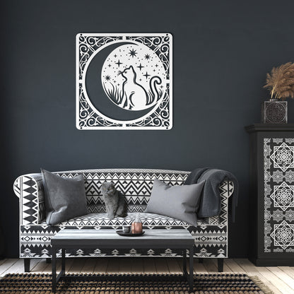 A white home decor metal sign of a cat inside a crescent moon next to a field of stars. All of this is bordered by floral vines. It hangs on the wall of a dark living room.