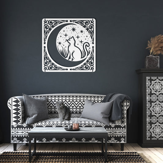 A white home decor metal sign of a cat inside a crescent moon next to a field of stars. All of this is bordered by floral vines. It hangs on the wall of a dark living room.